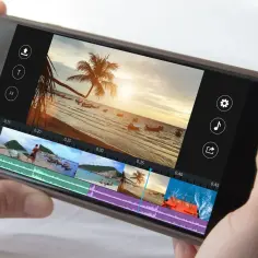 Smartfon z interfejsem programu do montowania filmów. Widok na plażę z palmą i łodziami.