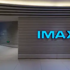 Jasnoniebieski napis IMAX na szarej, prążkowanej ścianie. To wejście do kina, gdzie czeka Cię niezapomniane wrażenie.