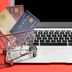 Miniaturowy wózek z kartami płatniczymi na klawiaturze laptopa. Takie zakupy na OLX to wygoda i bezpieczeństwo.