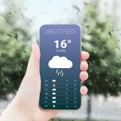 Dłoń trzyma smartfon z aplikacją pogodową pokazującą 16 stopni i deszcz. Prognoza na tydzień.