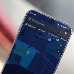 Na ekranie telefonu widać mapy googlr z zaznaczonym stadionem i opcjami wyszukiwania: stacje paliw, hotele, spożywcze, restauracje.
