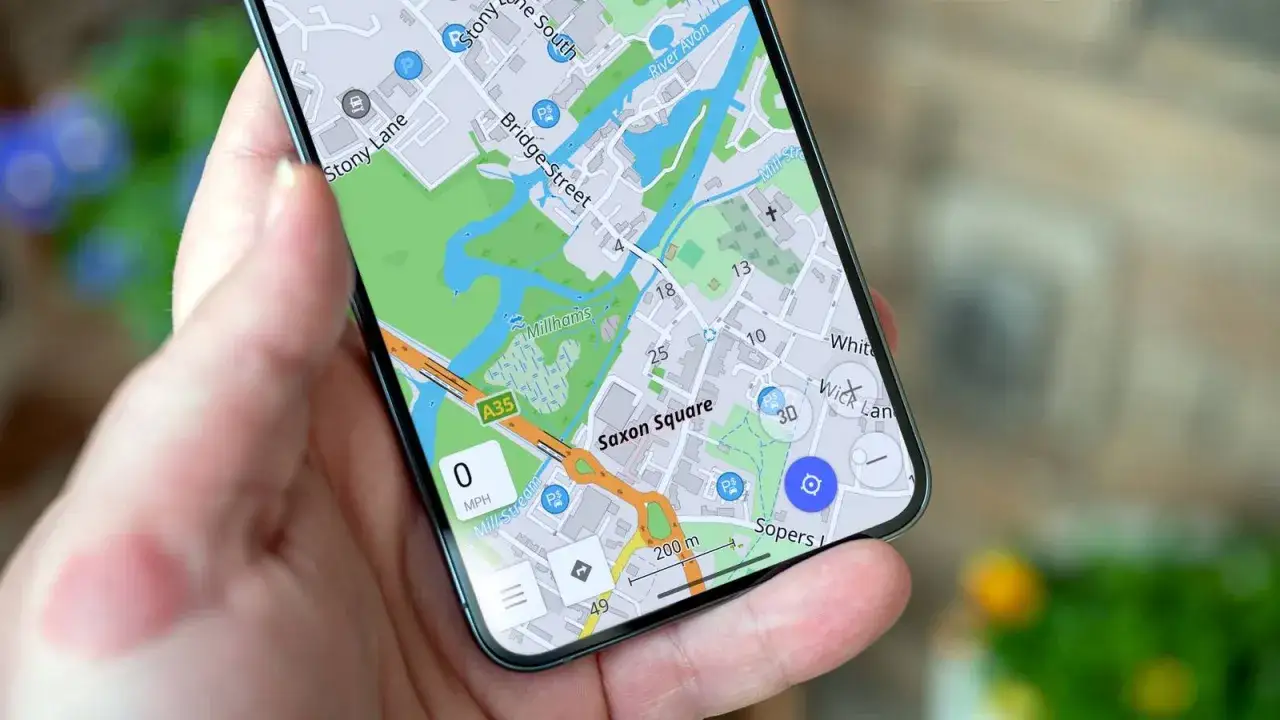 Dłoń trzyma smartfon z widokiem mapy, przypominającej mapy googlr. Widoczne nazwy ulic: Saxon Square, Stony Lane, Bridge Street.