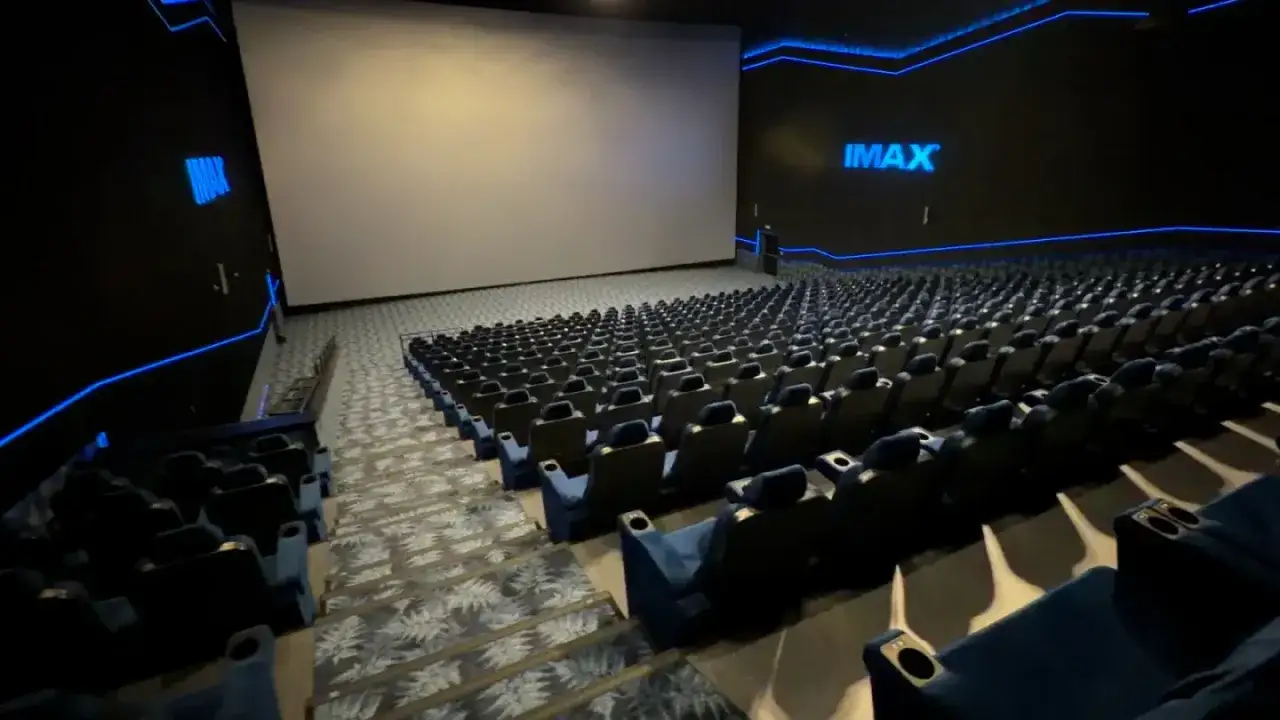 Pusta sala kinowa IMAX z dużym ekranem i rzędami niebieskich foteli. To właśnie imax co to za wrażenia!