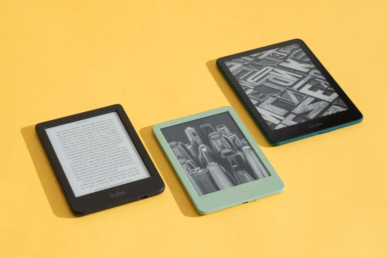 Trzy czytniki e-booków na żółtym tle. Jeden z nich, czarny Kobo, wyświetla tekst. Dwa pozostałe, zielony i turkusowy Kindle, pokazują grafiki. Idealne do czytania książek.