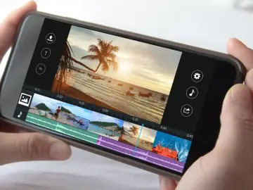 Smartfon z interfejsem programu do montowania filmów. Widok na plażę z palmą i łodziami.