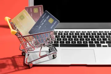 Miniaturowy wózek z kartami płatniczymi na klawiaturze laptopa. Takie zakupy na OLX to wygoda i bezpieczeństwo.